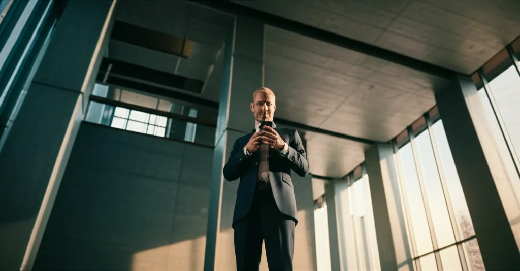 都心中古マンション価格の今後｜「ワニの口」が示す市場の変調 - 近代的なオフィスビルのロビーでスマートフォンを操作するスーツ姿の男性