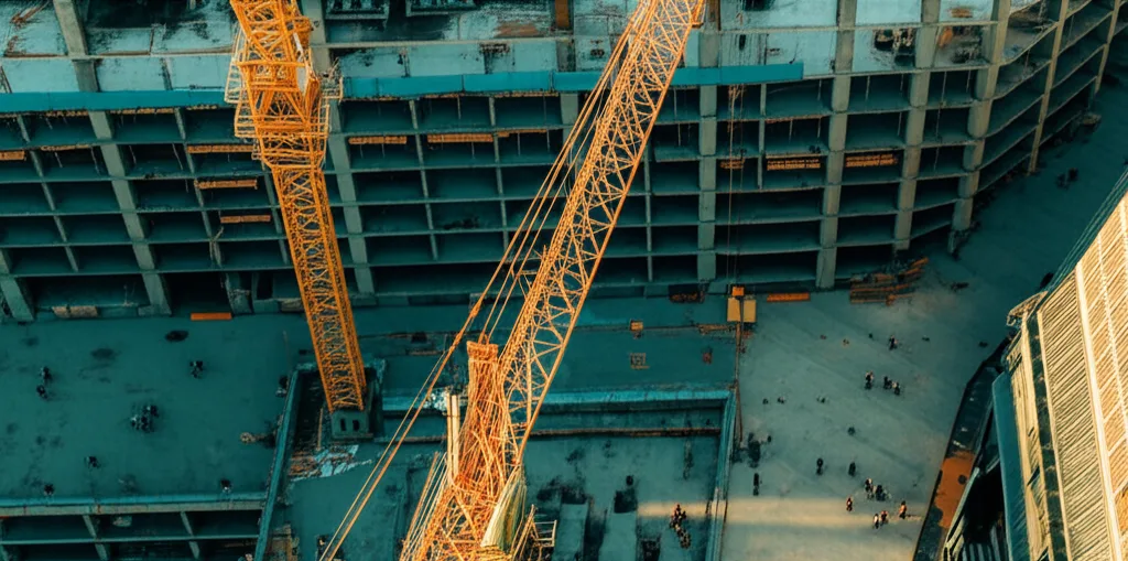 不動産投資2025年｜市場動向と会社員が取るべき戦略 - 再開発が進む駅前広場、タワークレーンと新しいビルの建設現場、行き交う人々